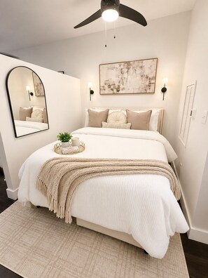 A bedroom with a bed, a ceiling fan, a wall-mounted mirror, a framed abstract painting, and a bedside table with a plant. - The Monroe Boutique Near Downtown (Atlanta)