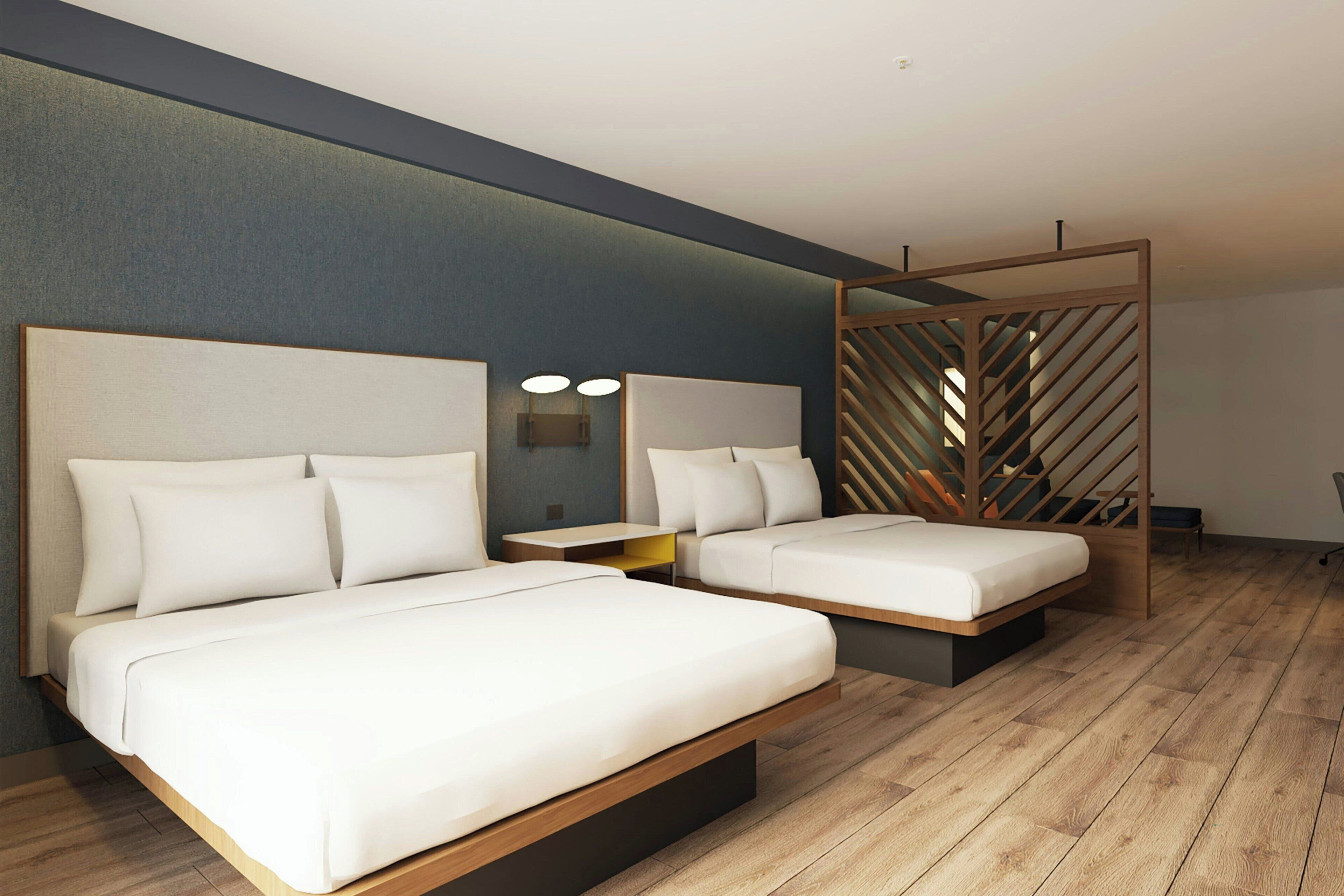 Una habitación de hotel moderna con dos camas, piso de madera, pared oscura y separador de madera.