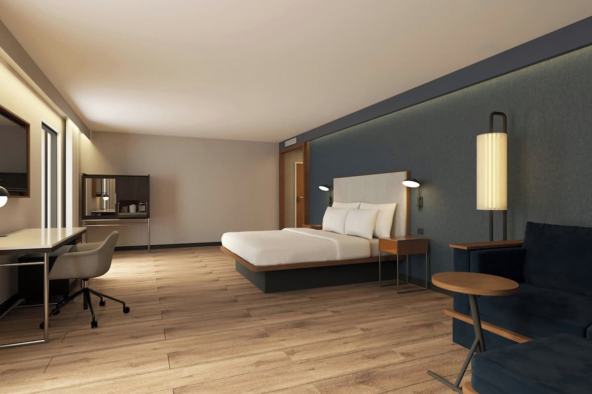 Una habitación de hotel moderna con cama, escritorio, silla y una pequeña mesa redonda.