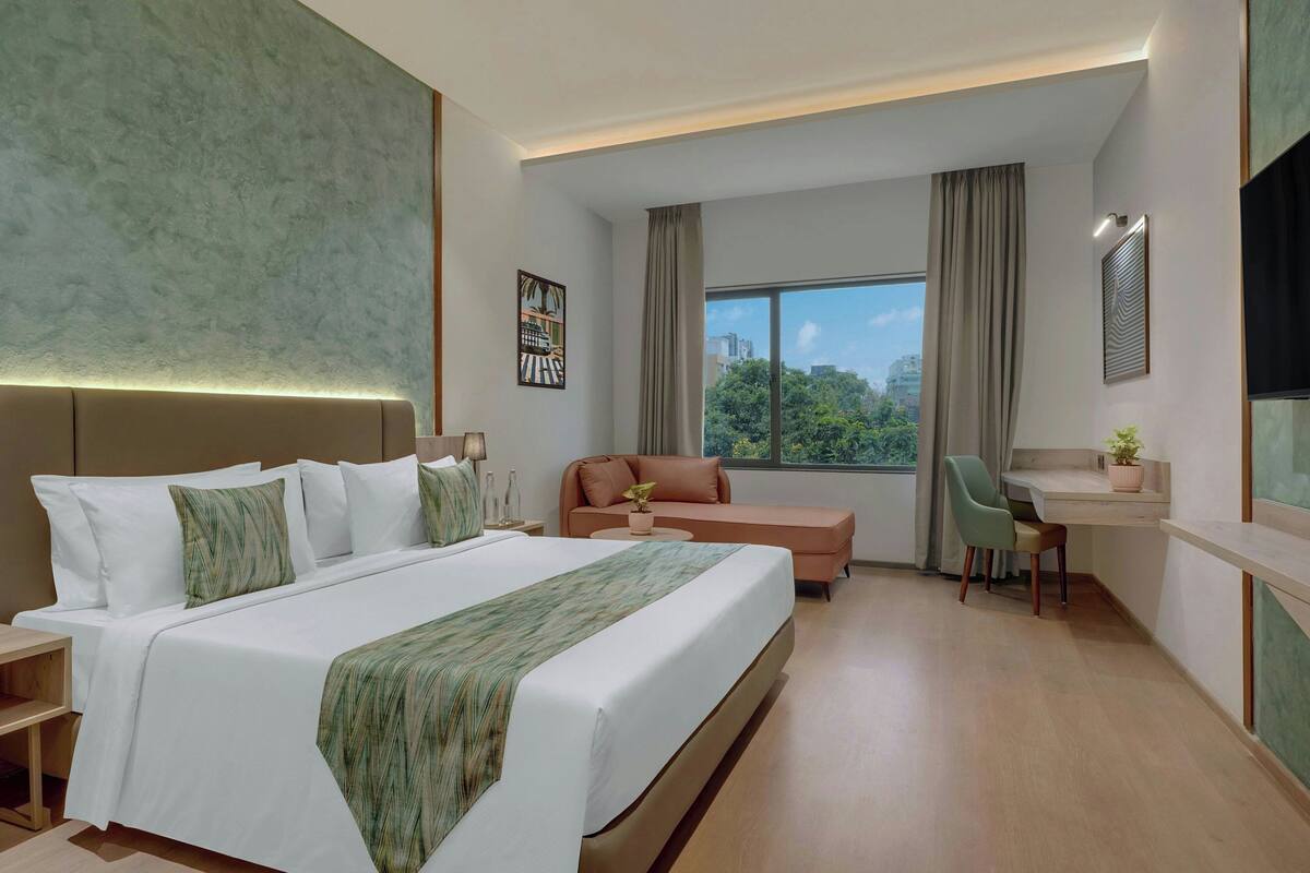 Quarto de hotel moderno com uma cama grande, uma escrivaninha, uma cadeira e vista para a cidade.
