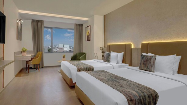 Een hotelkamer met twee bedden, een bureau, een stoel, een televisie en een raam met uitzicht op de stad.
