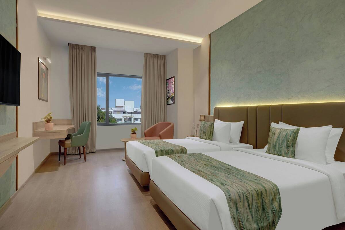 Quarto de hotel com duas camas, uma escrivaninha, uma cadeira, uma janela com vista e uma televisão de tela plana.