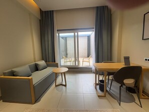 Una sala de estar moderna con un sofá, una mesita redonda, una mesa de comedor con sillas y vistas a través de un ventanal grande.