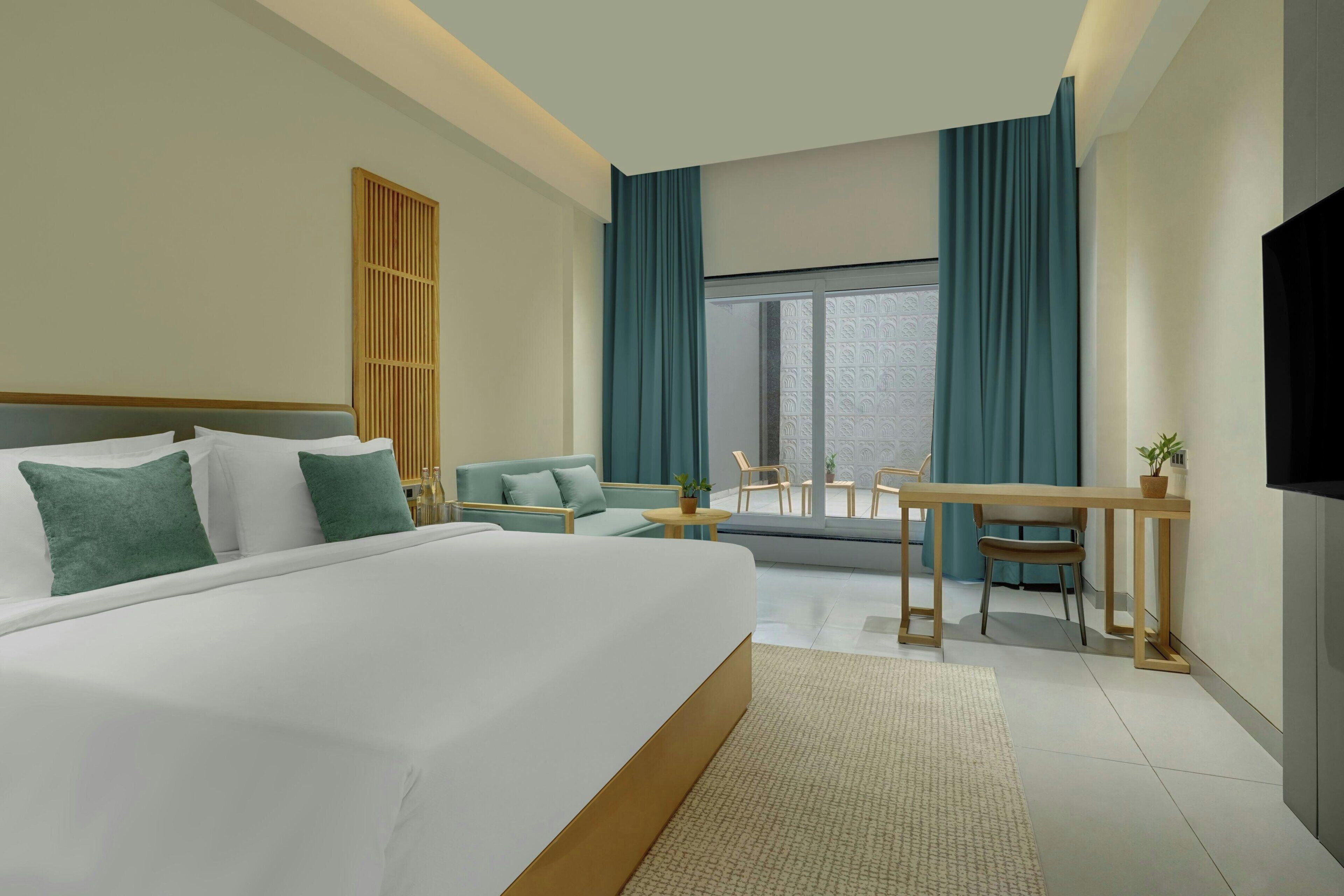 Habitación de hotel con una cama grande, zona de estar con mesa y sillas, televisor y ventana con cortinas.