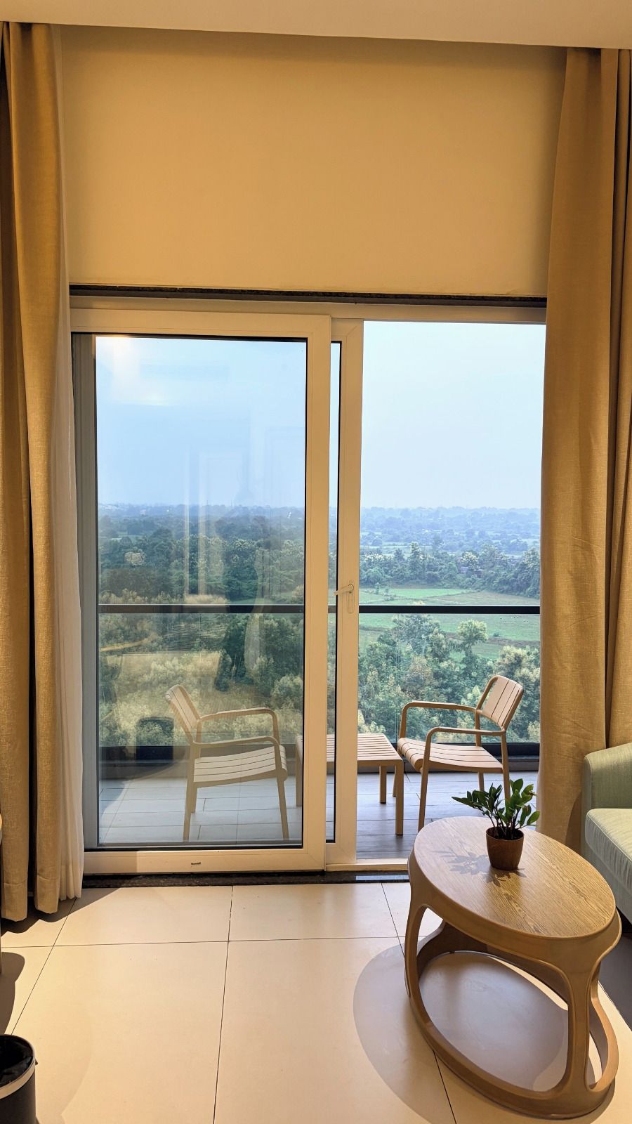 Un balcón con vistas a un paisaje verde, una silla de madera, una mesita y una planta en maceta.