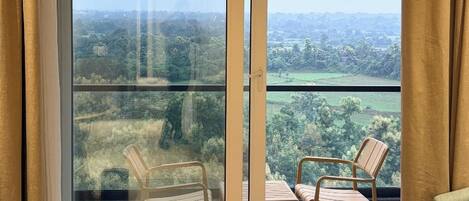 A balcony with a view of a green landscape, a wooden chair, a small table, and a potted plant.