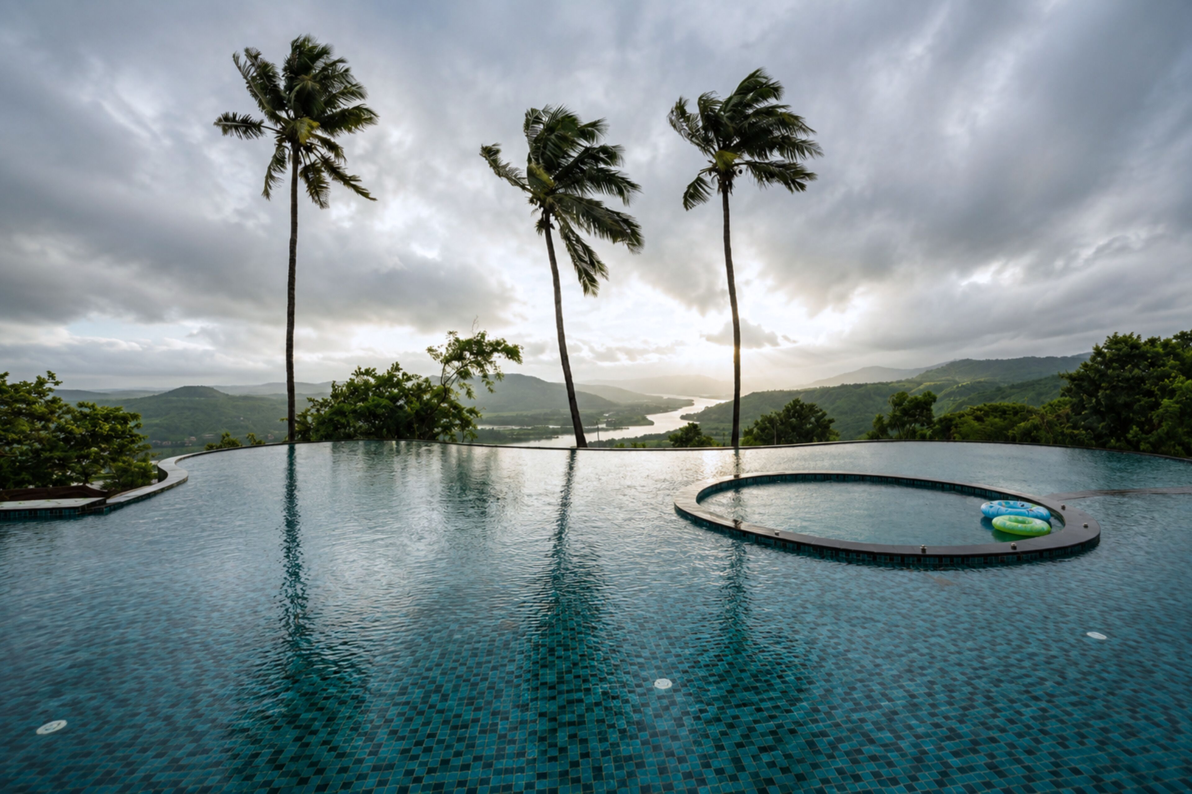 A infinity pool with a view of palm trees and a river.