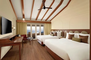 A hotel room with two beds, a TV, a desk, a chair, and a view of the outdoors.