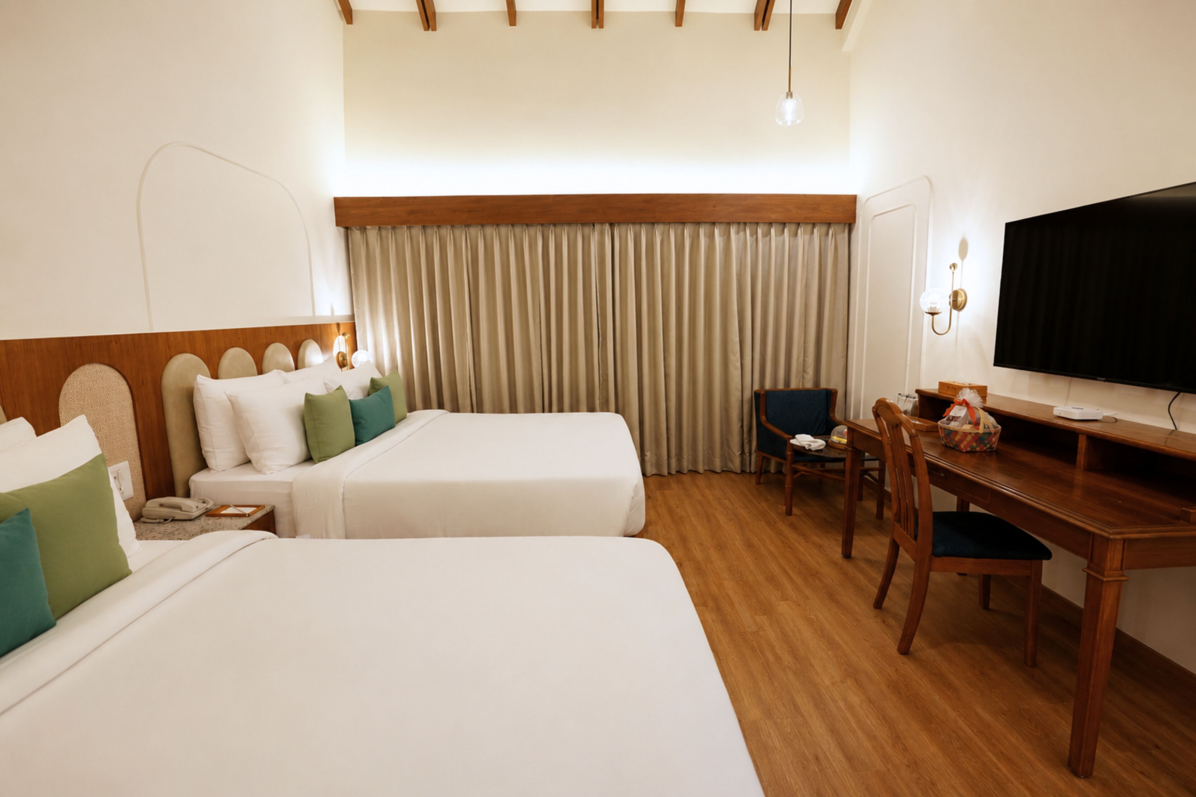 Ein Hotelzimmer mit zwei Betten, einem Schreibtisch, einem Stuhl, einem Fernseher und einem Fenster mit Vorhängen.