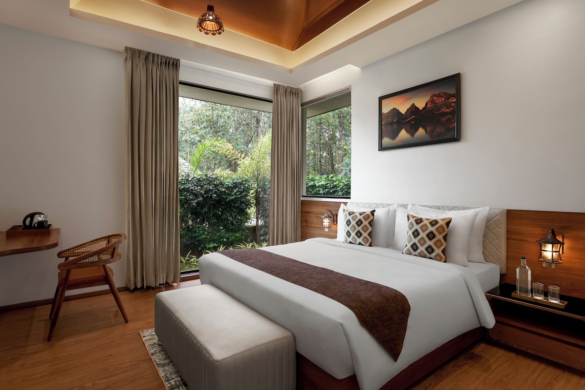 A modern bedroom with a large bed, a desk, and a view of greenery.