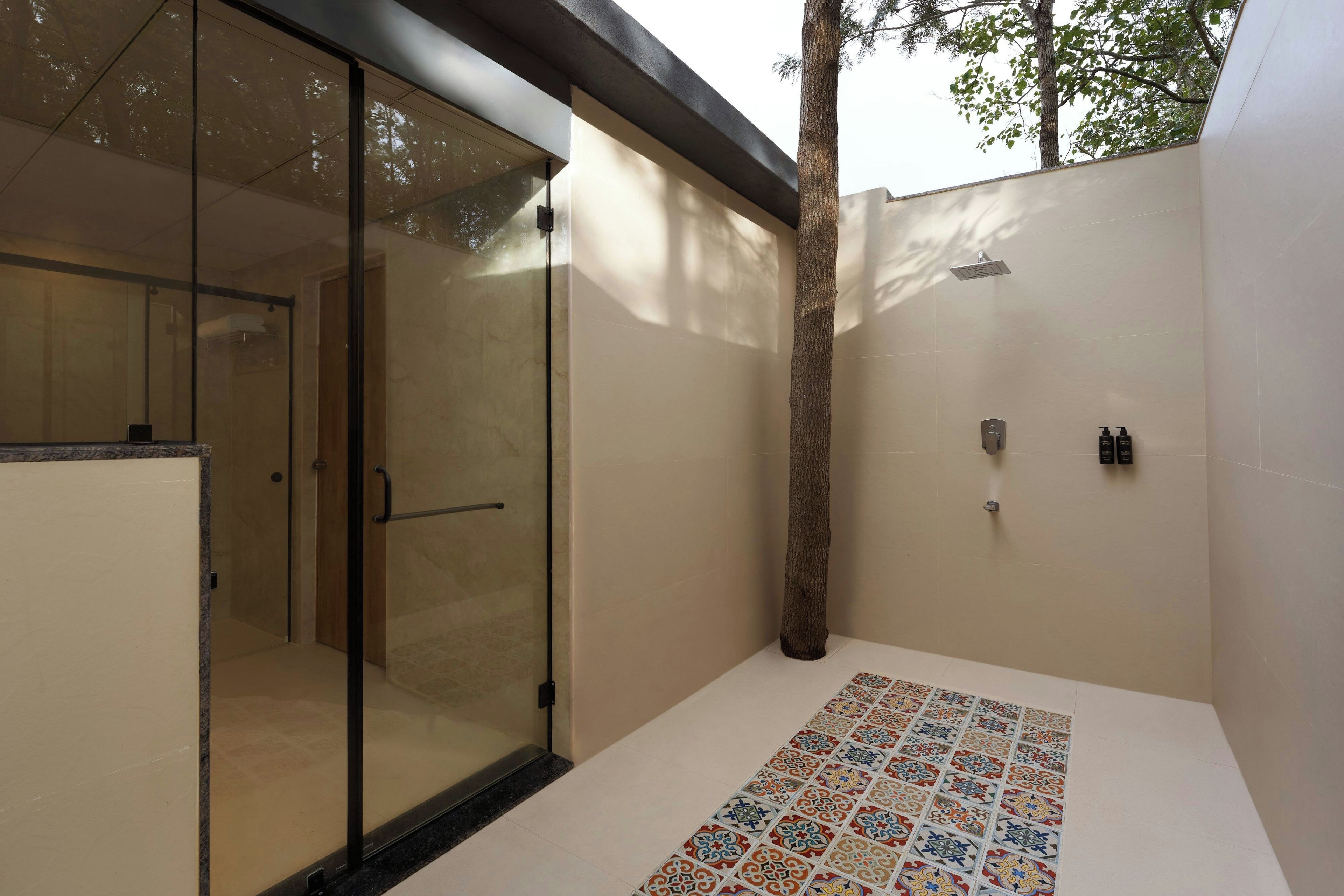 Un baño moderno con cabina de ducha de vidrio, suelo de baldosas con un estampado colorido y un árbol a la vista.