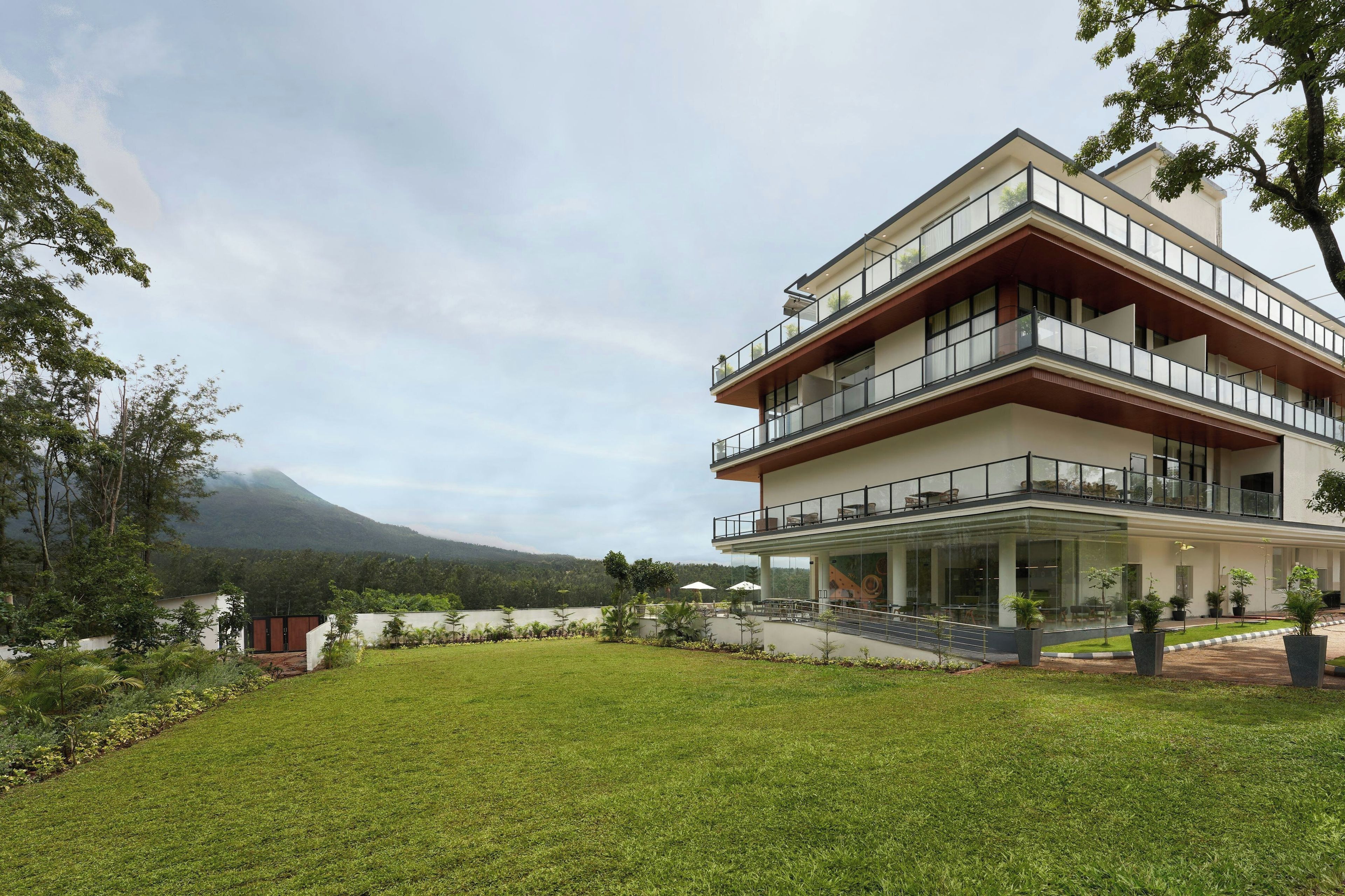 A modern multi-story building with a flat roof, large glass windows, and a balcony with outdoor seating.