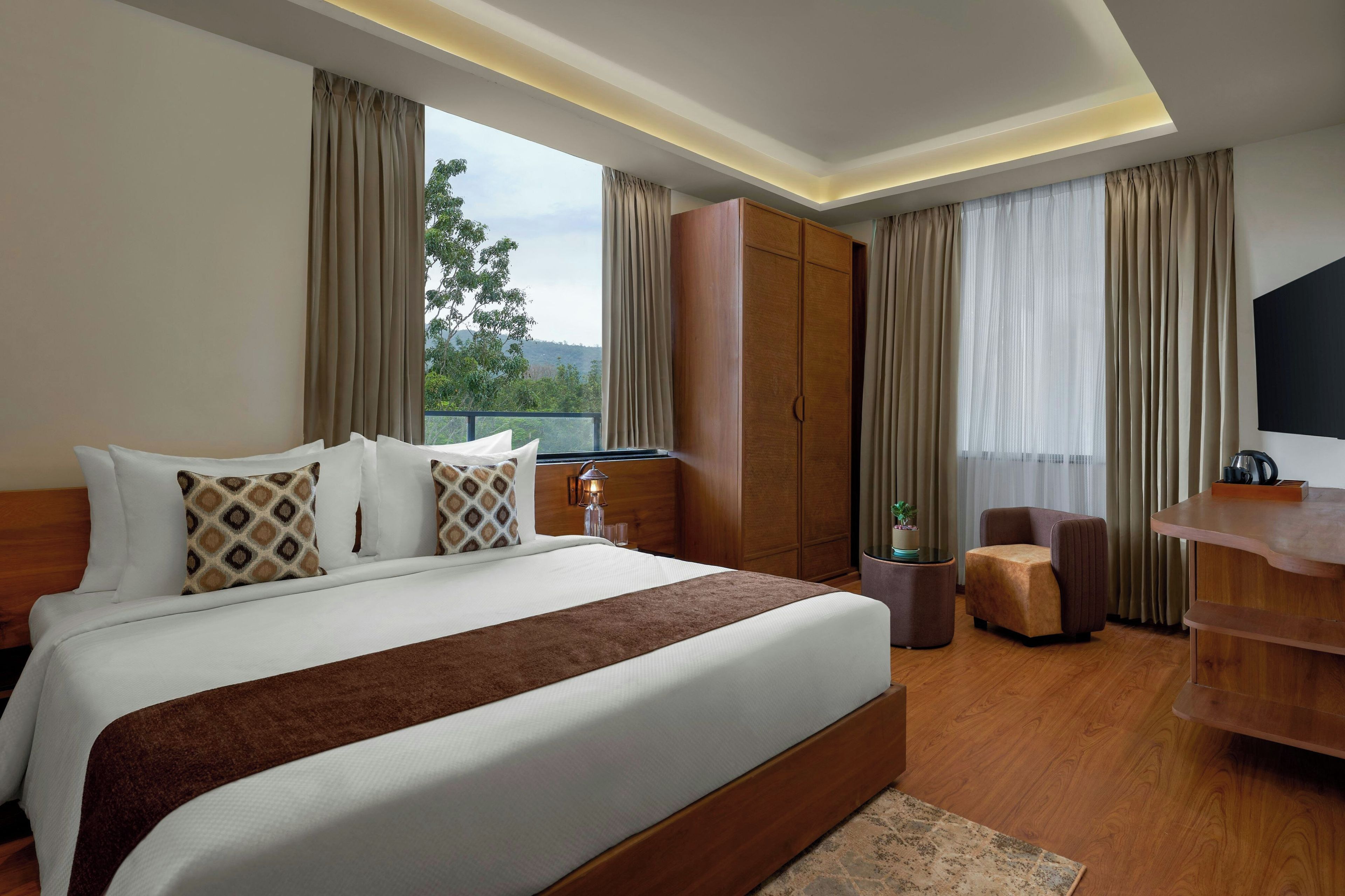 A hotel room with a large bed, a wooden wardrobe, a seating area, and a television.