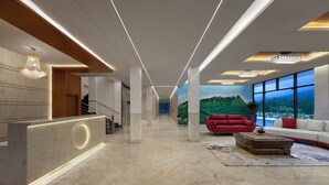 En modern entréhall med en receptionsdisk, en trappa, en röd soffa och ett stort fönster med utsikt över bergen.