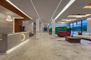 A modern lobby with a reception desk, a staircase, a red sofa, and a large window with a mountain view. - Ug The Fern Resort & Spa Chikmagalur, Series By Marriott (Chikkamagaluru)