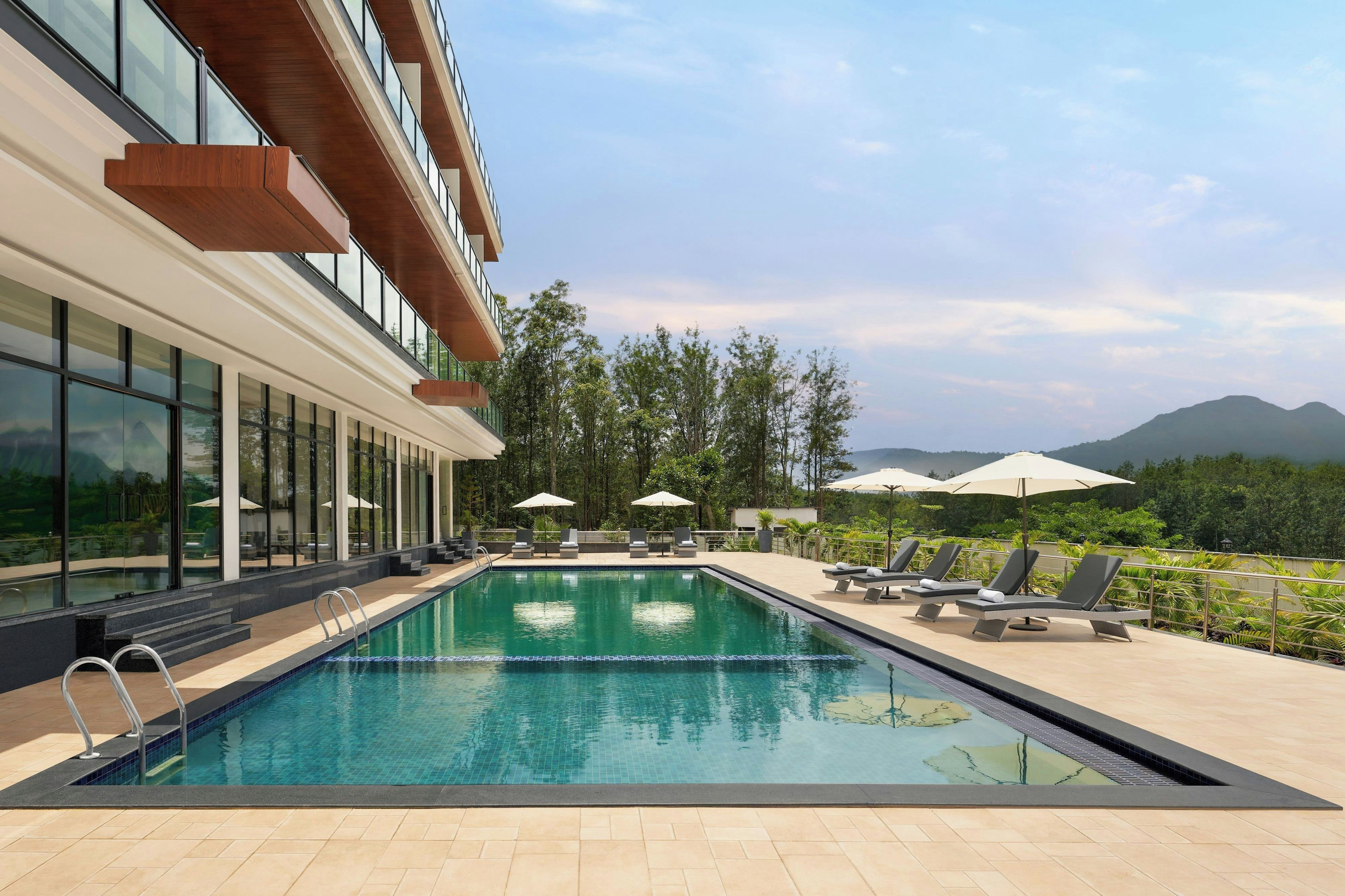 A modern hotel with a swimming pool, lounge chairs, and a view of the mountains.