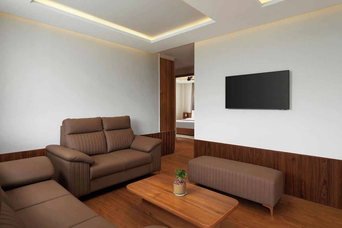 Een moderne woonkamer met een bruine leren bank, een houten salontafel en een aan de muur bevestigde televisie.