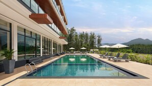 En swimmingpool med solstolar och parasoller, omgiven av en byggnad med stora fönster och utsikt över bergen.