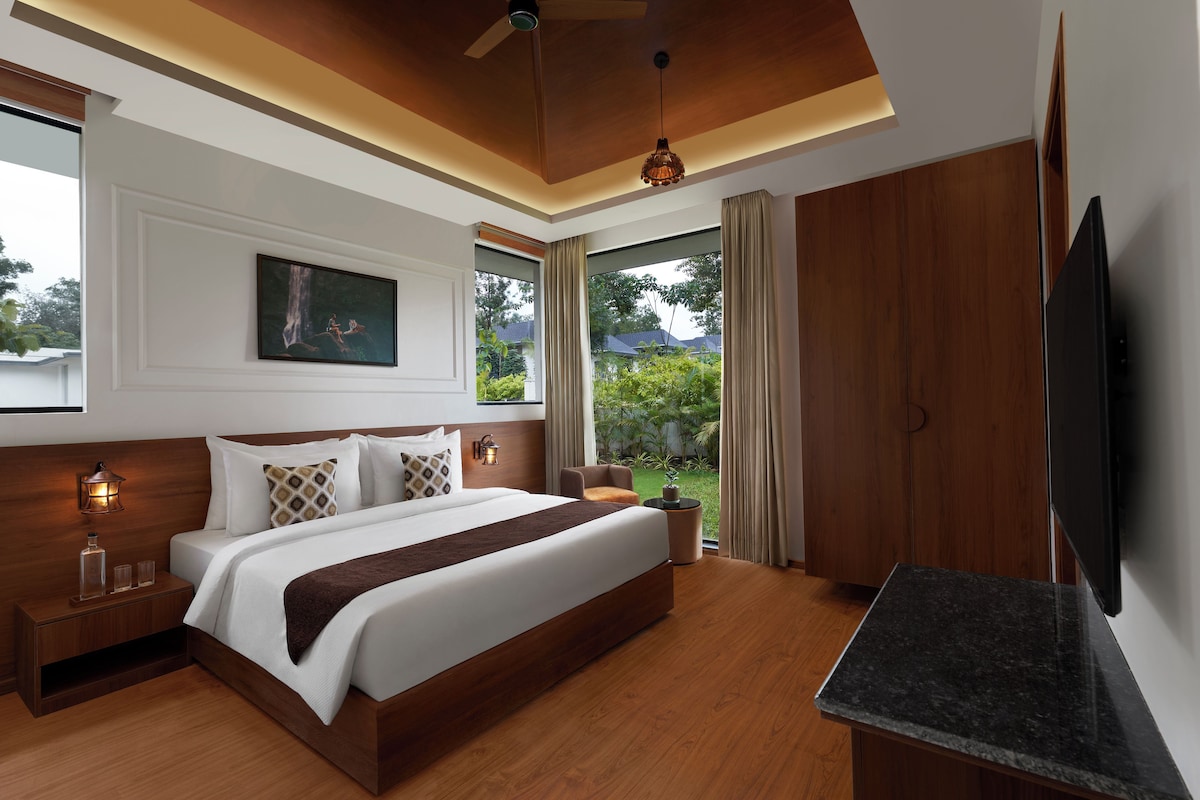 A modern bedroom with a large bed, a flat-screen TV, and a view of a garden.