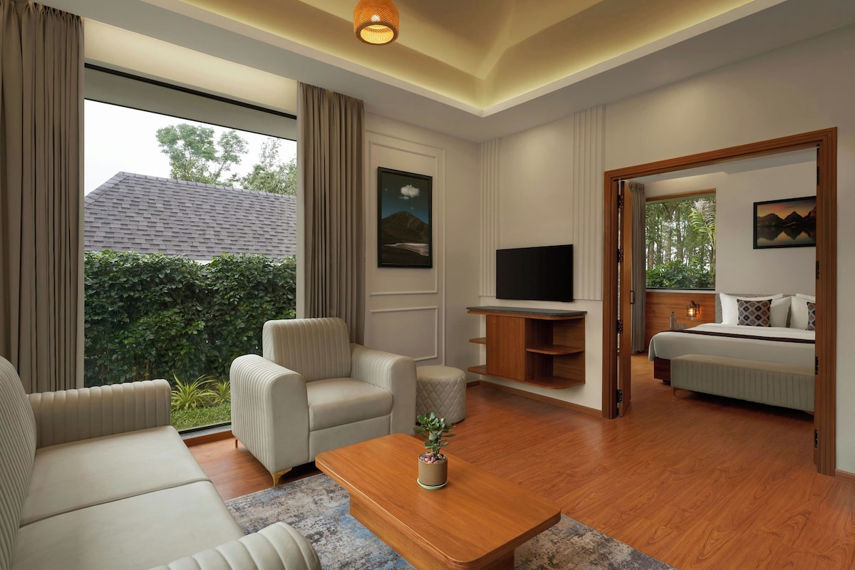 Een moderne woonkamer met een bank, fauteuils, een salontafel, een televisie en een slaapkamer met een bed en nachtkastje.