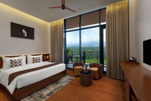 A modern hotel room with a large bed, a ceiling fan, a view of the outdoors, and a balcony with outdoor furniture. - Ug The Fern Resort & Spa Chikmagalur, Series By Marriott (Chikkamagaluru)