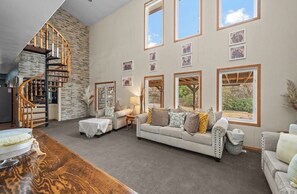 A spacious living room with a stone accent wall, a spiral staircase, and large windows with framed pictures. - 5 bed / 4.5 bath, large entertaining luxury home w/reservoir access nearby (Pueblo)