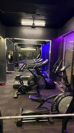 Een sportschool met diverse loopbanden, hometrainers en een spiegelwand.