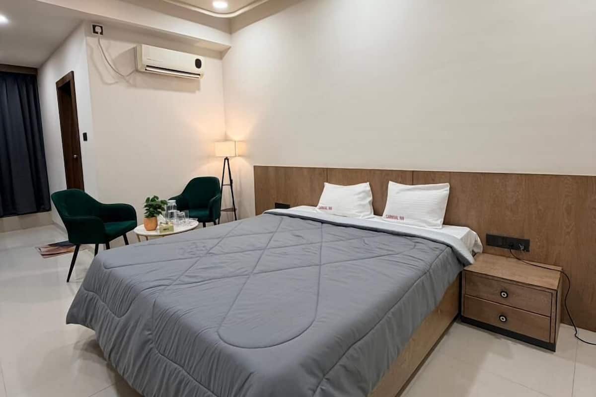 A modern hotel room with a large bed, a ceiling fan, a bedside table, and a small desk with a chair.