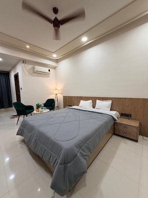 A modern hotel room with a large bed, a ceiling fan, a bedside table, and a small desk with a chair.