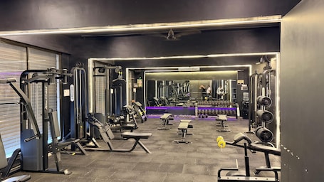A gym with various exercise equipment, a mirrored wall, and a bench area.. Carnival Inn