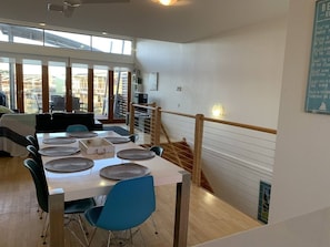 A dining area with a table set for six, chairs, and a view of the outdoors through large windows.