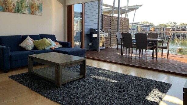 A modern living room with a sofa, coffee table, and a view of a deck and outdoor area. - Villa #91 South Shores ~ The golden hour (Normanville)