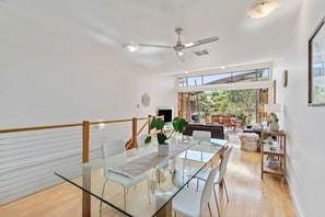 A spacious dining area with a glass table, white chairs, and a view of the outdoors.