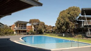 A swimming pool with a surrounding deck, adjacent buildings, and trees. - Villa #41 South Shores ~ Dune side escape (Normanville)
