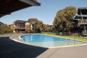 A swimming pool with a surrounding deck, adjacent buildings, and trees.