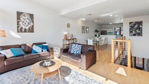 A modern living room with a brown leather sofa, a small wooden coffee table, and a dining area in the background. - Villa #41 South Shores ~ Dune side escape (Normanville)