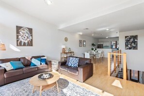 A modern living room with a brown leather sofa, a small wooden coffee table, and a dining area in the background.