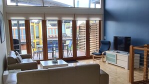 Un salon avec un canapé, un téléviseur et une vue sur un espace extérieur, accessible par de grandes portes vitrées.