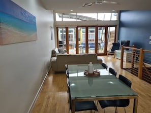 A modern room with a glass table, a sofa, and a view through large glass doors to an outdoor area. - Villa #13 South Shores ~ Water facing escape (Normanville)