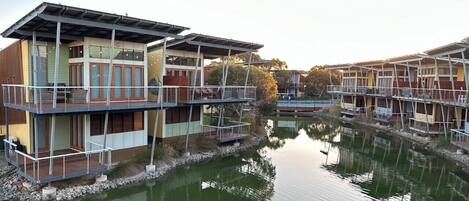 A waterfront property with multiple buildings, each featuring balconies and a reflective water body in the foreground.