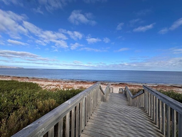 A wooden boardwalk leading to a beach with a clear sky.
