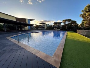 A swimming pool with a wooden deck and artificial grass.