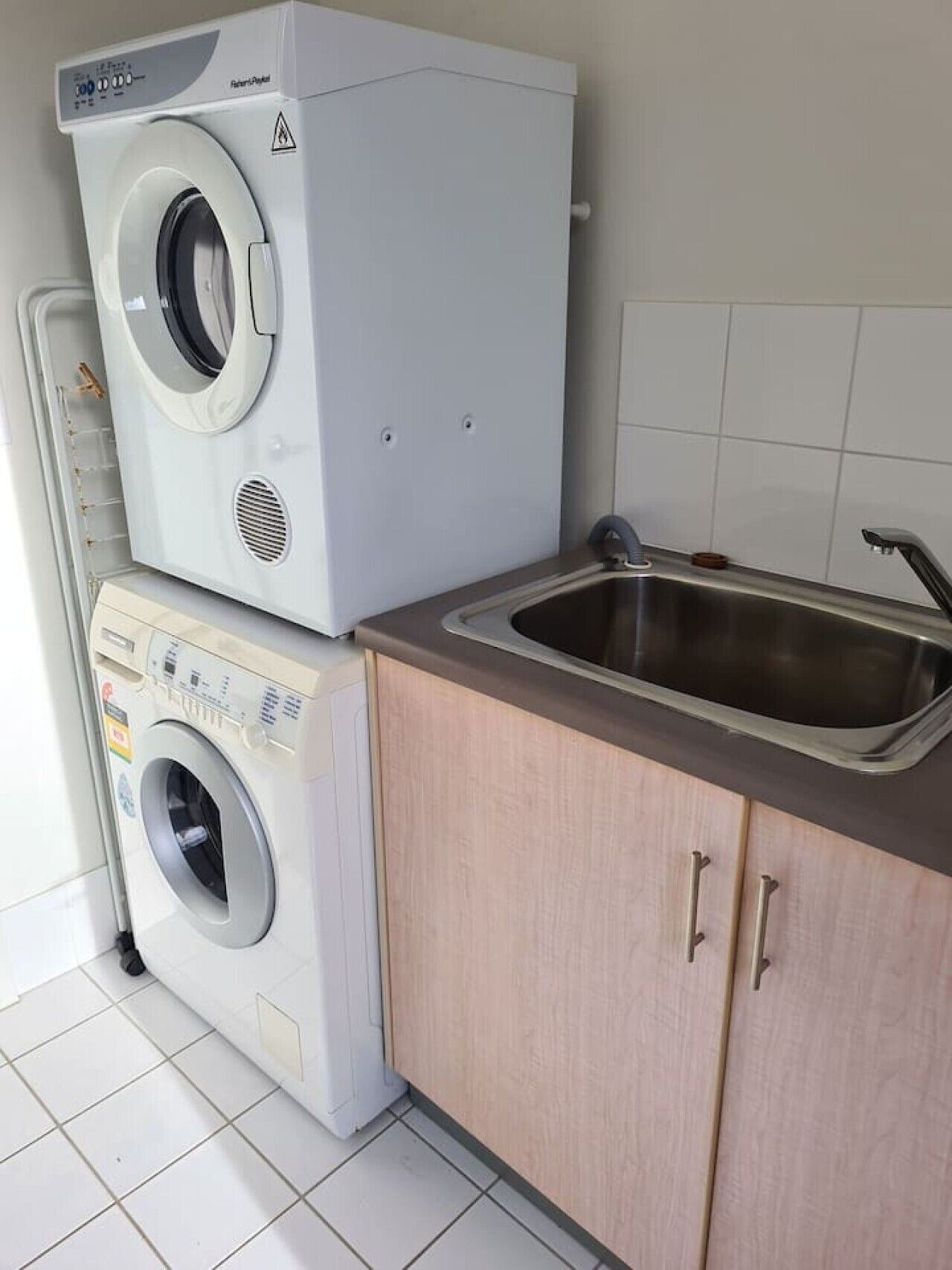 Un espace buanderie équipé d’un lave-linge à chargement par le haut et d’un sèche-linge à chargement frontal, d’un évier en acier inoxydable et de meubles de couleur claire.