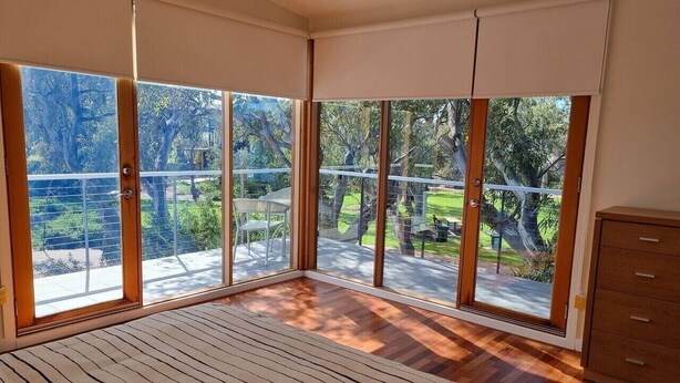 A bedroom with large windows, a bed, and a wooden dresser.