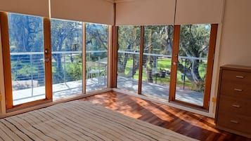 A bedroom with large windows, a bed, and a wooden dresser.