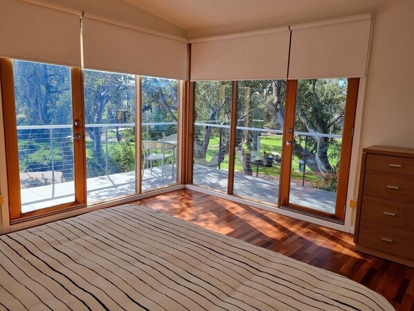 A bedroom with large windows, a bed, and a wooden dresser.