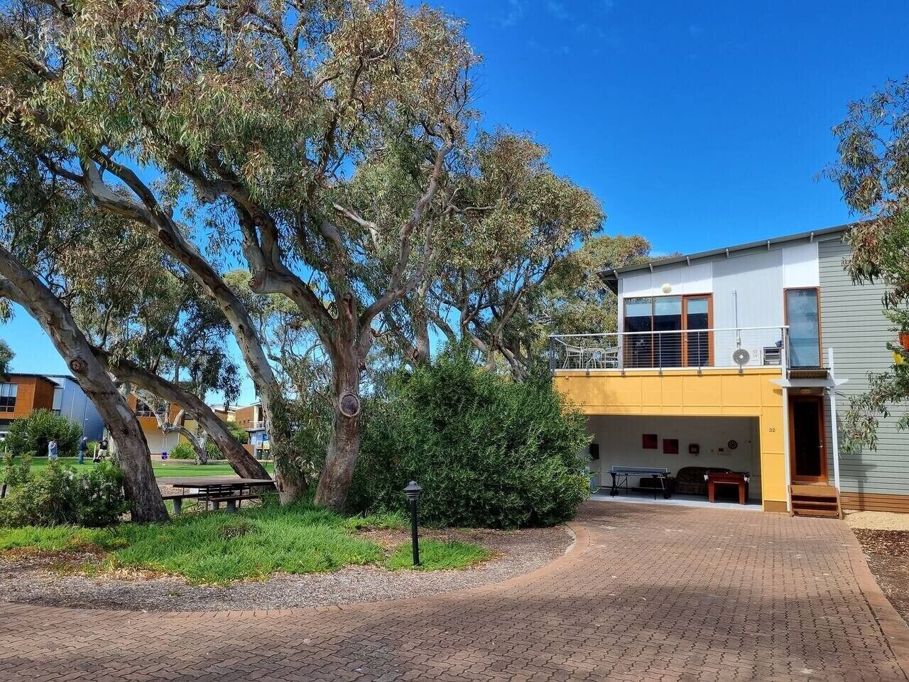 Un bâtiment à deux étages doté d’un espace extérieur couvert, d’une allée pavée et d’arbres adultes.