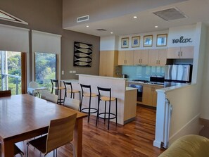 A modern kitchen with a central island, wooden flooring, and a dining area with a table and chairs.