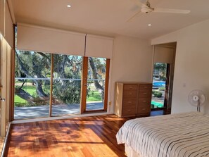 A bedroom with a large sliding glass door leading to a balcony, a wooden dresser, and a ceiling fan.