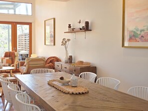 A dining area with a wooden table, white chairs, a woven placemat, and a vase with dried flowers.